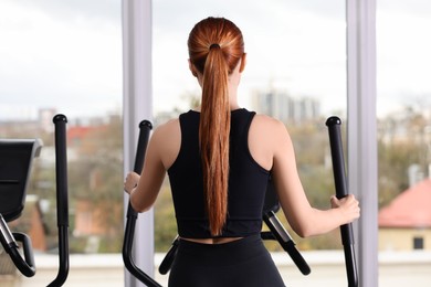 Photo of Athletic woman doing exercise with air walker in gym, back view