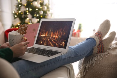 MYKOLAIV, UKRAINE - DECEMBER 25, 2020: Woman with sweet drink watching Harry Potter and Philosopher's stone movie on laptop at home, closeup. Cozy winter holidays atmosphere
