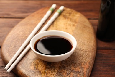 Bowl with soy sauce and chopsticks on wooden table, closeup