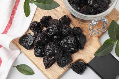 Photo of Tasty dried prunes and green leaves on light table, top view