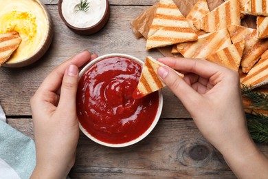 Photo of Woman dipping pita chip into sauce at wooden table, top view