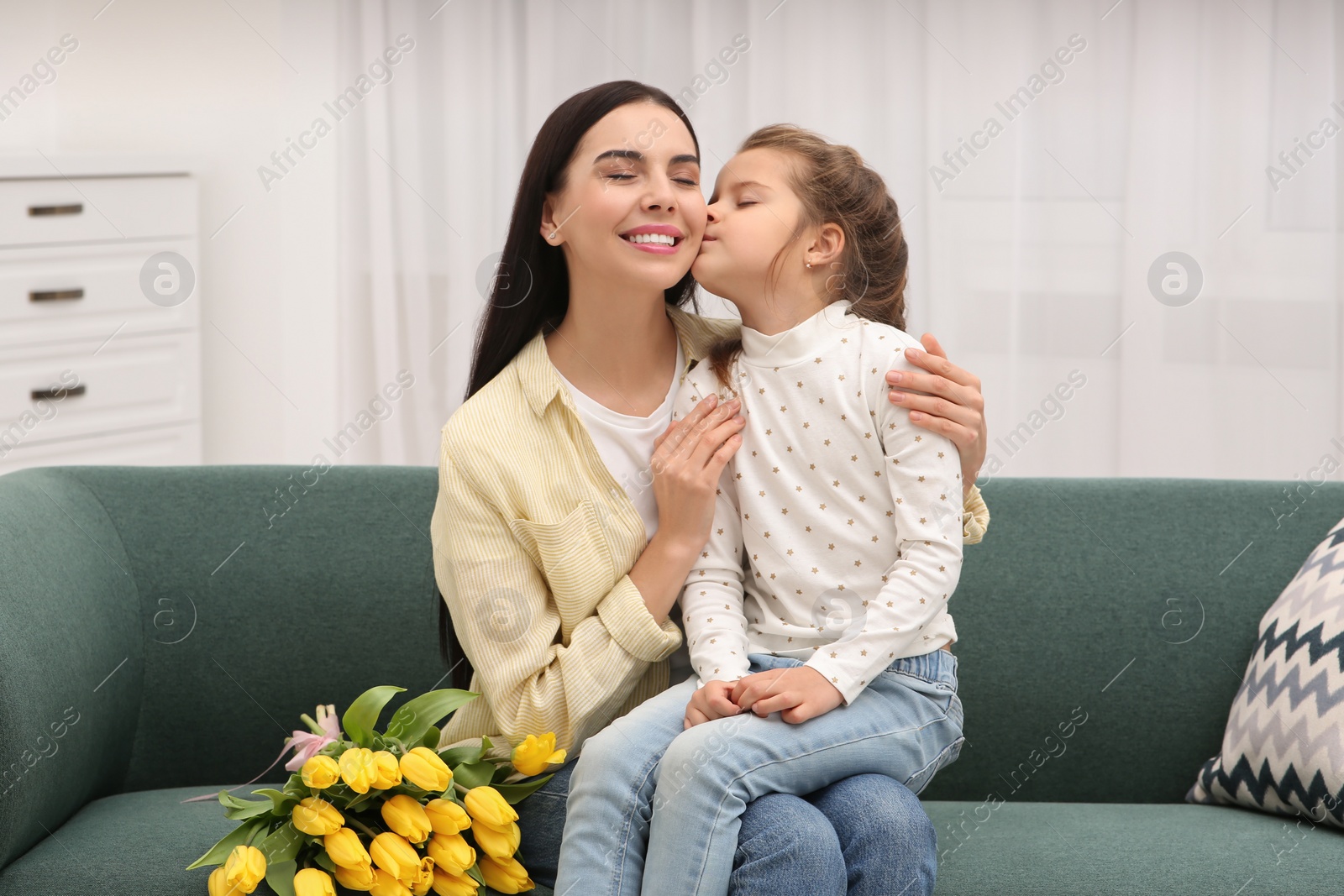 Photo of Happy woman and her cute daughter with bouquet of yellow tulips on sofa at home. Mother's day celebration