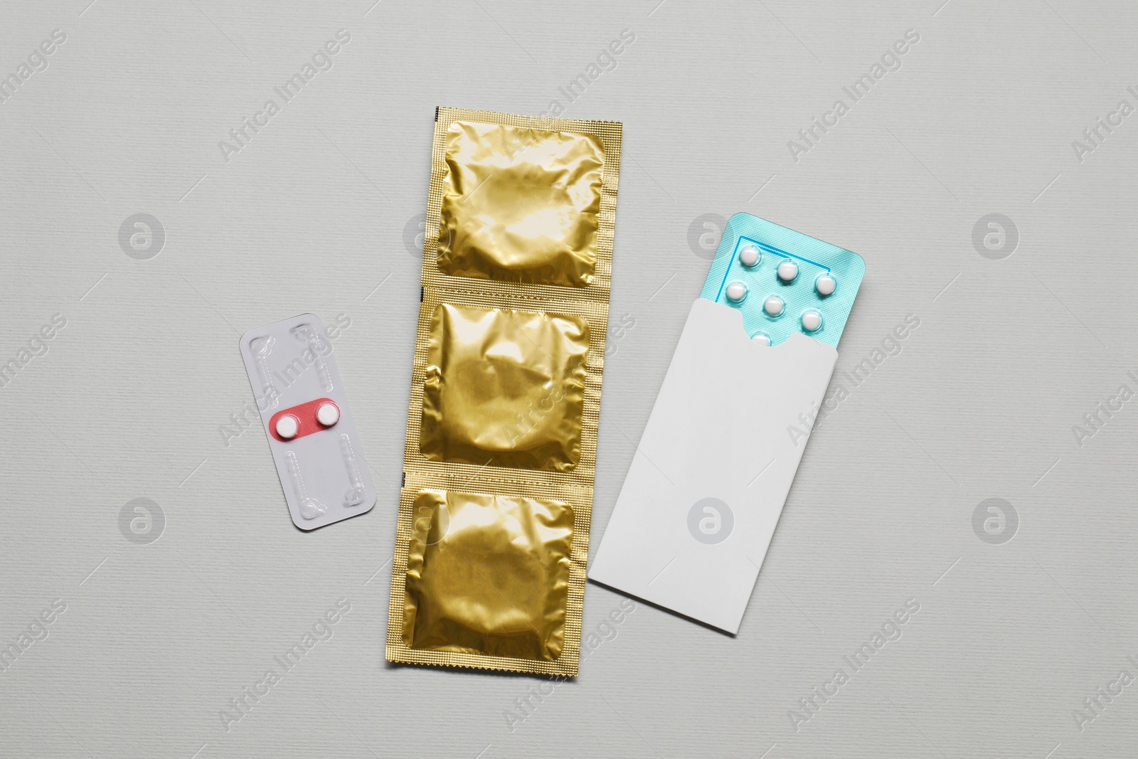 Photo of Contraception choice. Pills and condoms on light grey background, flat lay