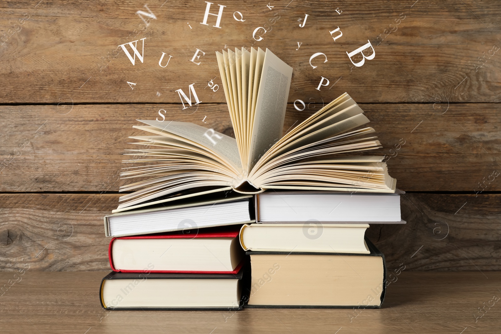 Image of Open book with letters flying out of it on wooden background