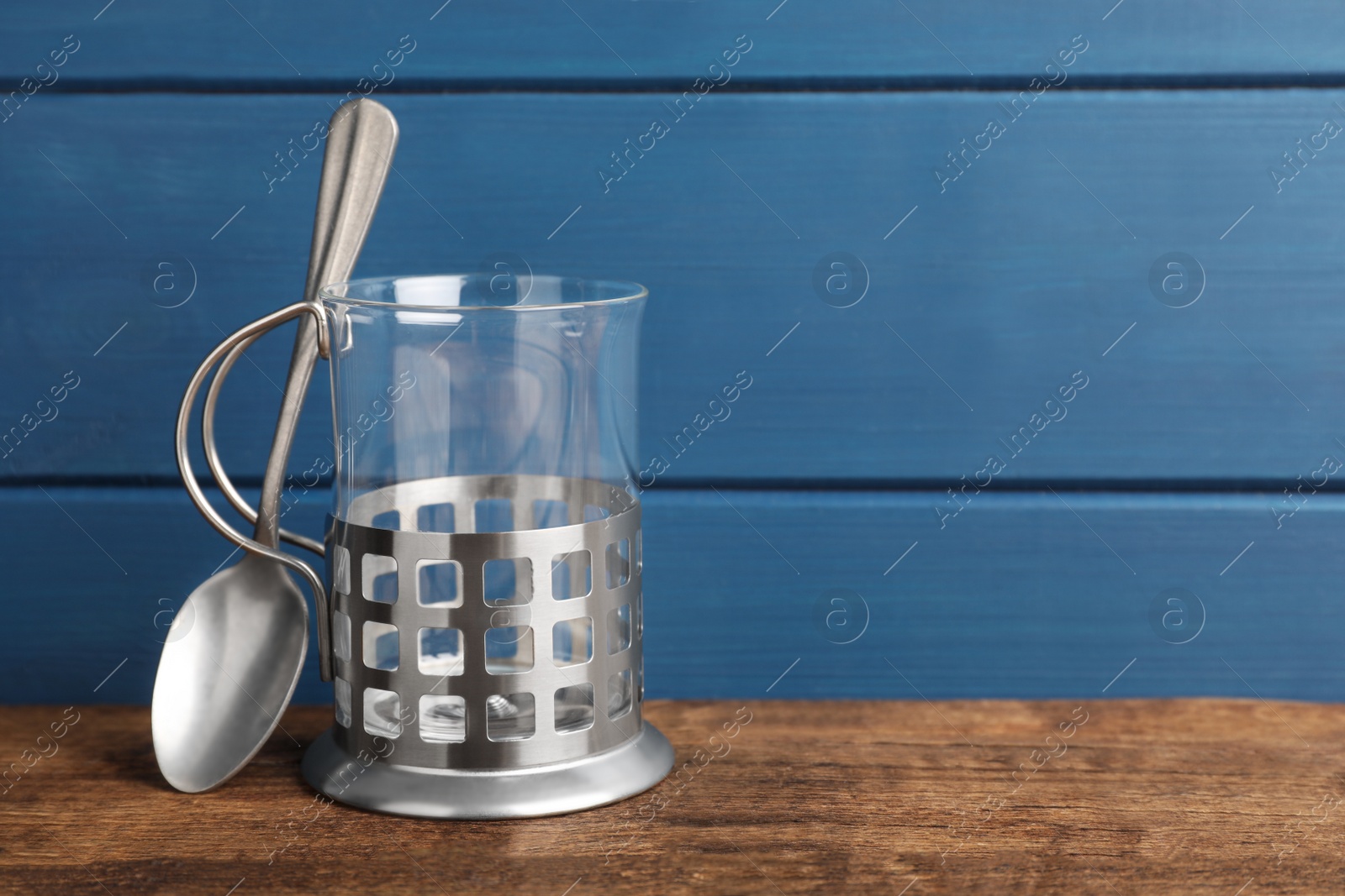 Photo of Traditional tea glass holder and spoon on wooden table against blue background, space for text