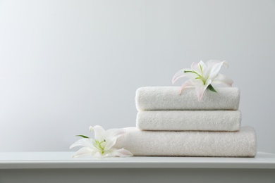 Stack of fresh towels with flowers on table against white background. Space for text