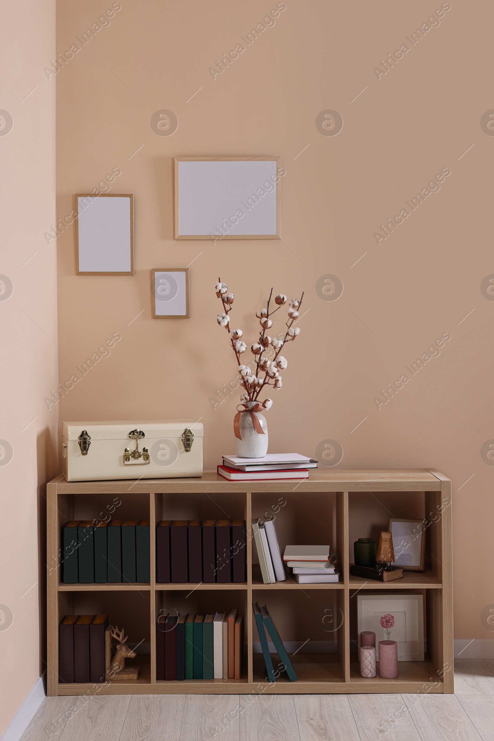 Photo of Vase with beautiful bouquet of white fluffy cotton flowers on wooden bookcase in cozy room. Interior design