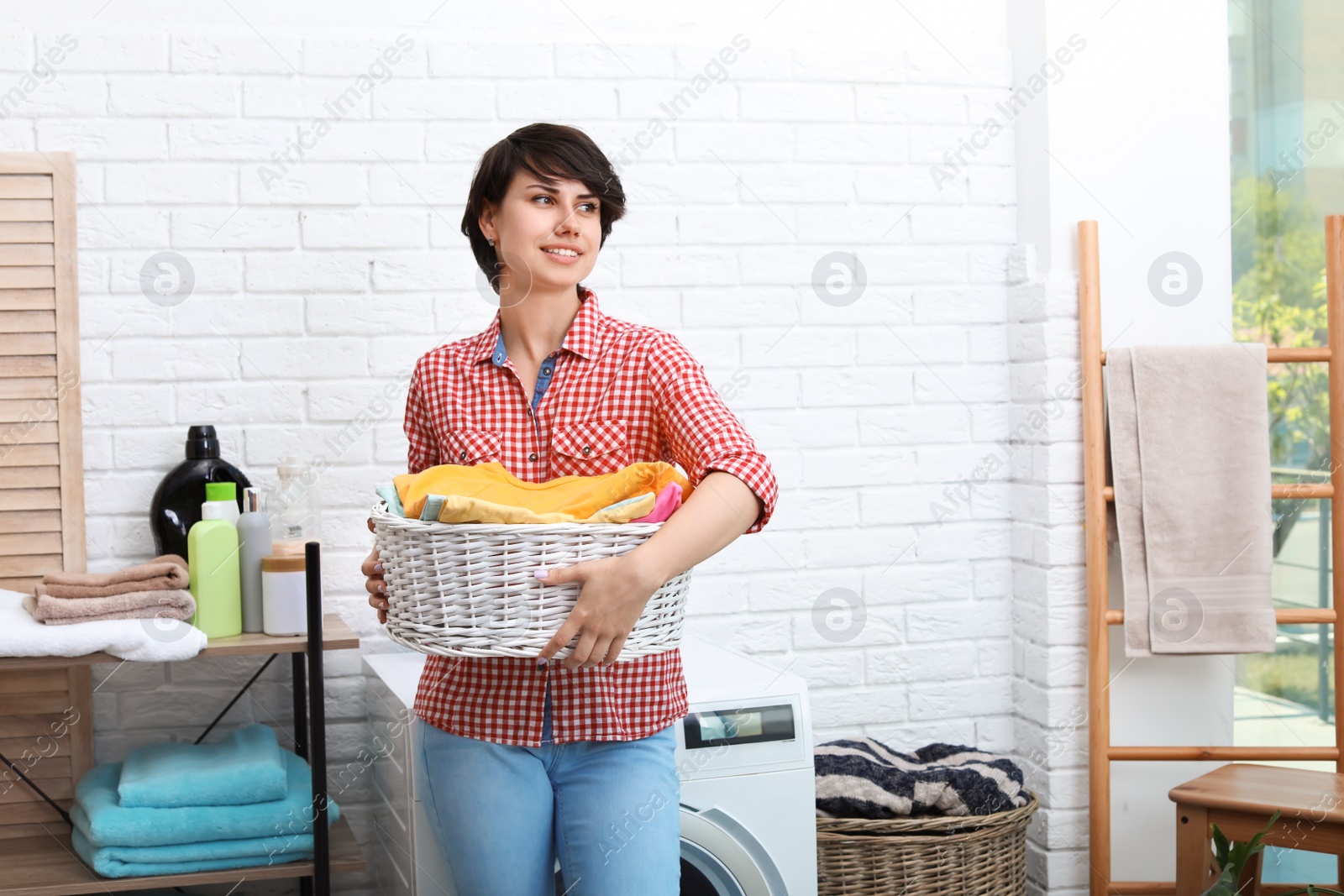 Photo of Young woman holding basket with clean clothes at home