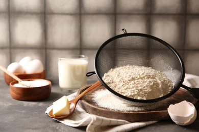 Photo of Making dough. Flour in sieve, spoon and butter on grey textured table, closeup