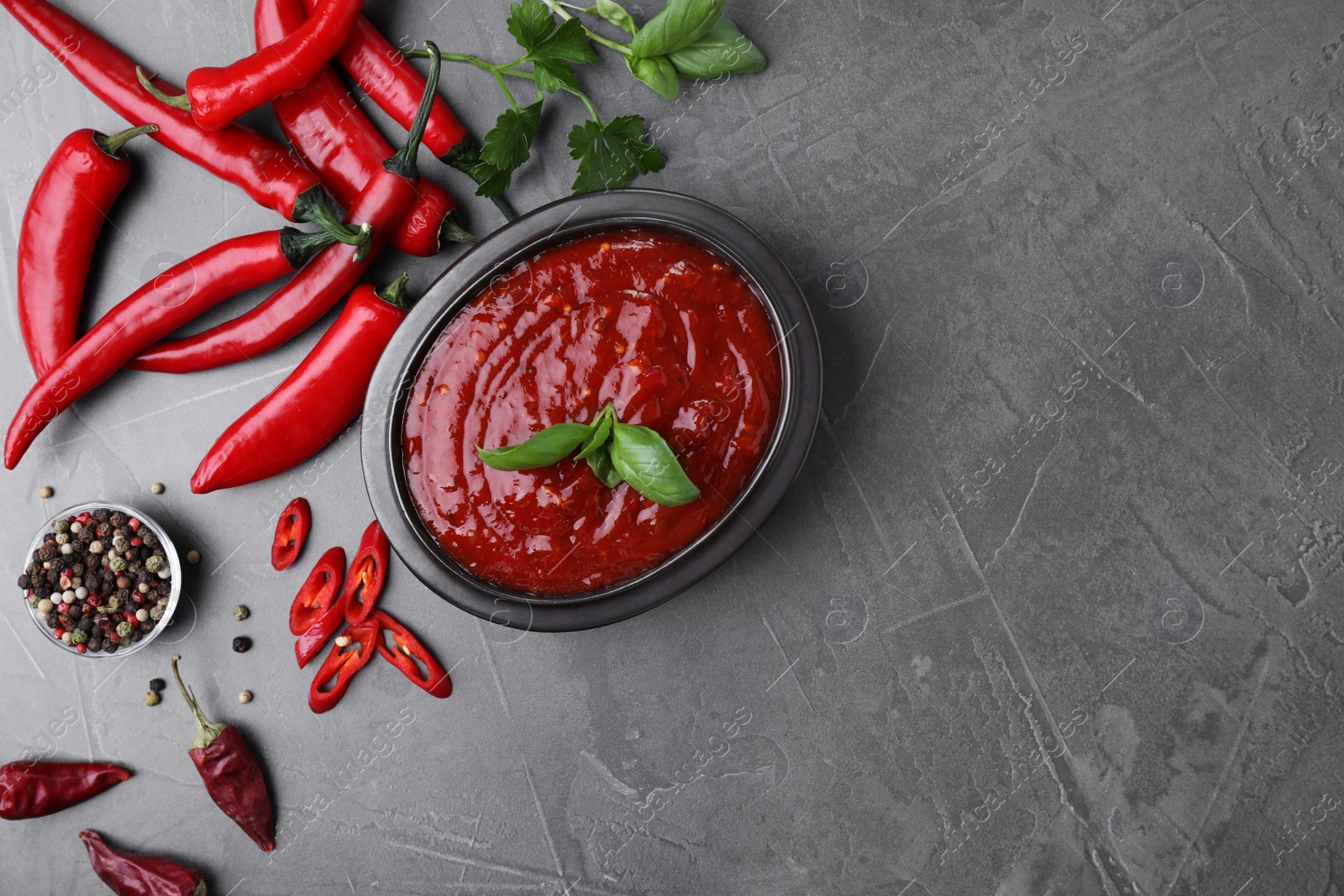 Photo of Flat lay composition with bowl of chili sauce and ingredients on grey table. Space for text