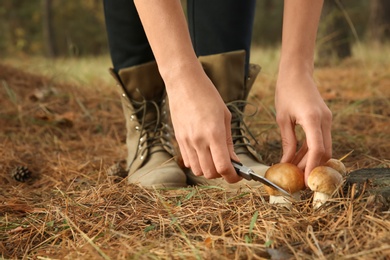 Photo of Woman cutting porcini mushroom with knife in forest, closeup