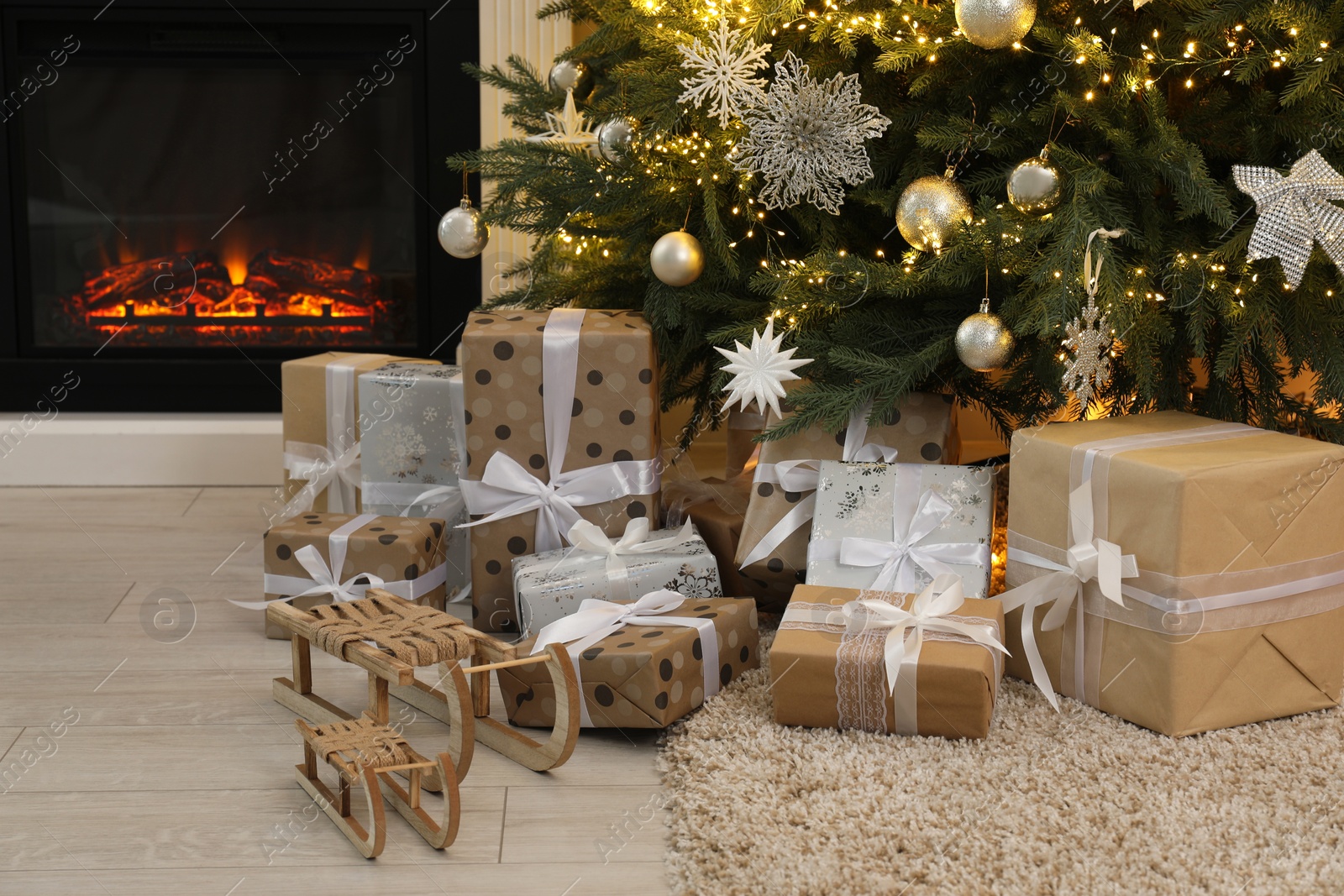 Photo of Many gift boxes and decorative sleighs under beautiful Christmas tree near fireplace at home