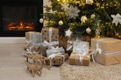 Many gift boxes and decorative sleighs under beautiful Christmas tree near fireplace at home