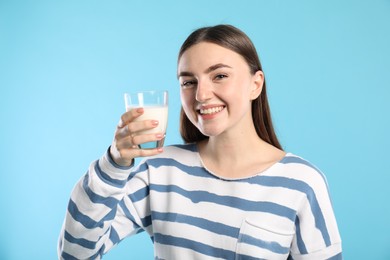 Happy woman with milk mustache holding glass of tasty dairy drink on light blue background