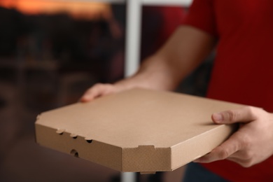 Courier with pizza box on blurred background, closeup. Space for text