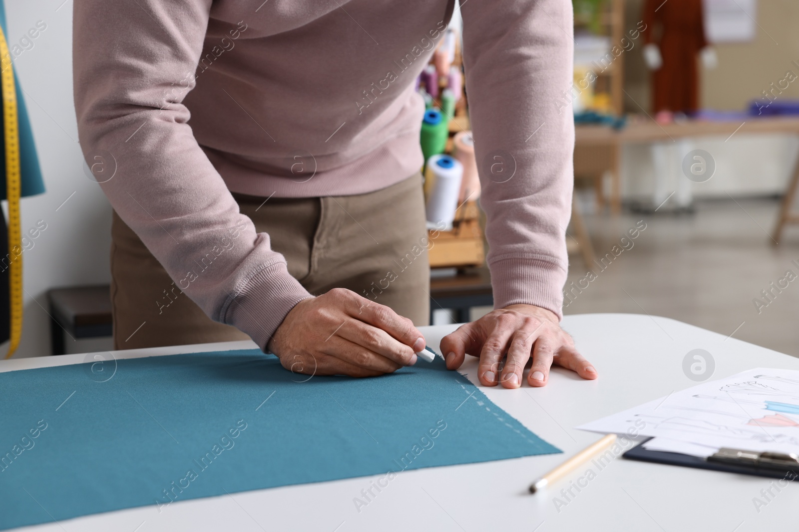 Photo of Dressmaker marking fabric with chalk in workshop, closeup