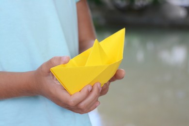 Little girl holding yellow paper boat outdoors, closeup