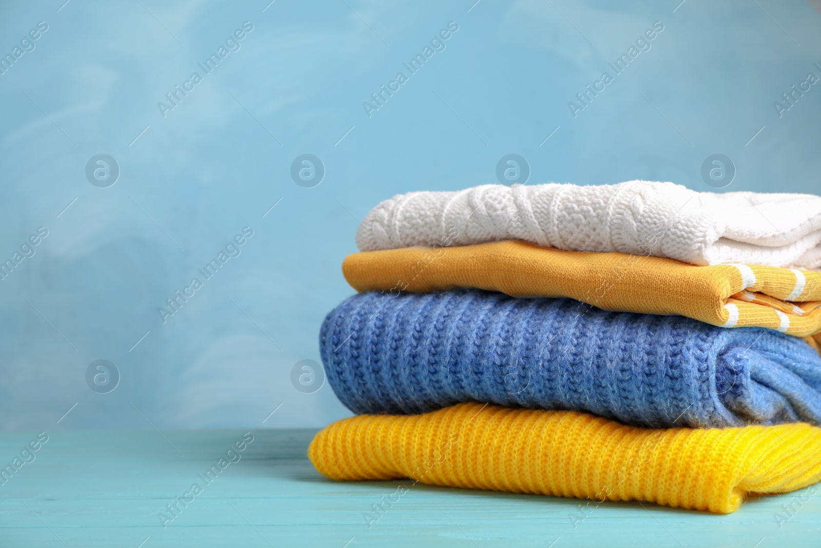 Photo of Stack of folded knitted sweaters on table. Space for text