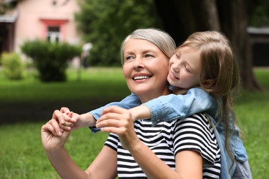 Happy grandmother with her granddaughter spending time together in park, space for text
