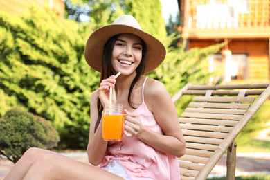 Image of Young woman with refreshing drink resting in deck chair outdoors