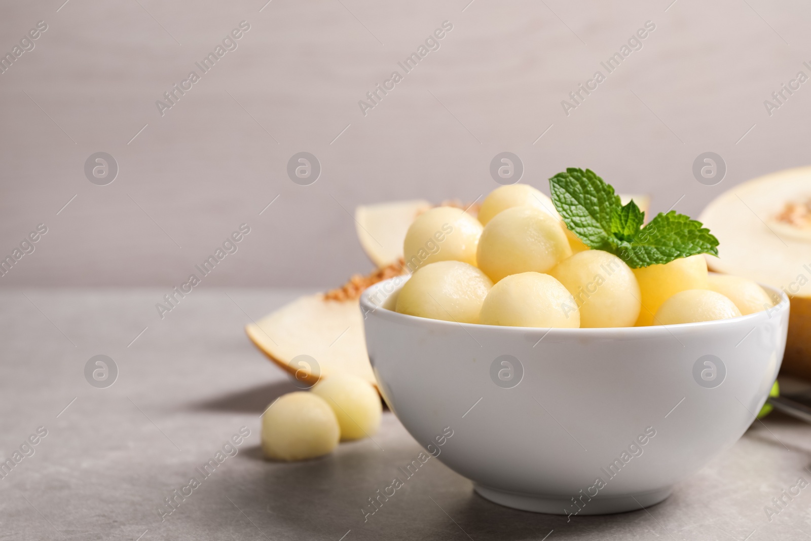 Photo of Melon balls and mint in bowl on light grey table, space for text