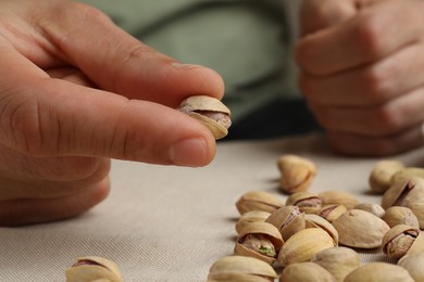 Woman holding tasty roasted pistachio nut at table, closeup