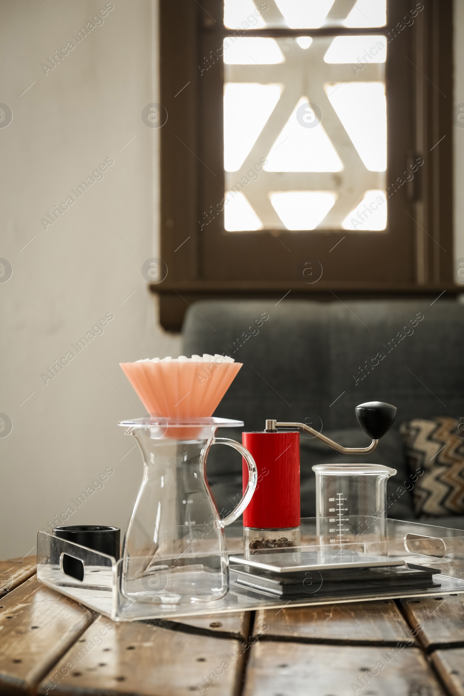 Photo of Manual coffee grinder with beans, glass jug and wave dripper on wooden table in cafe