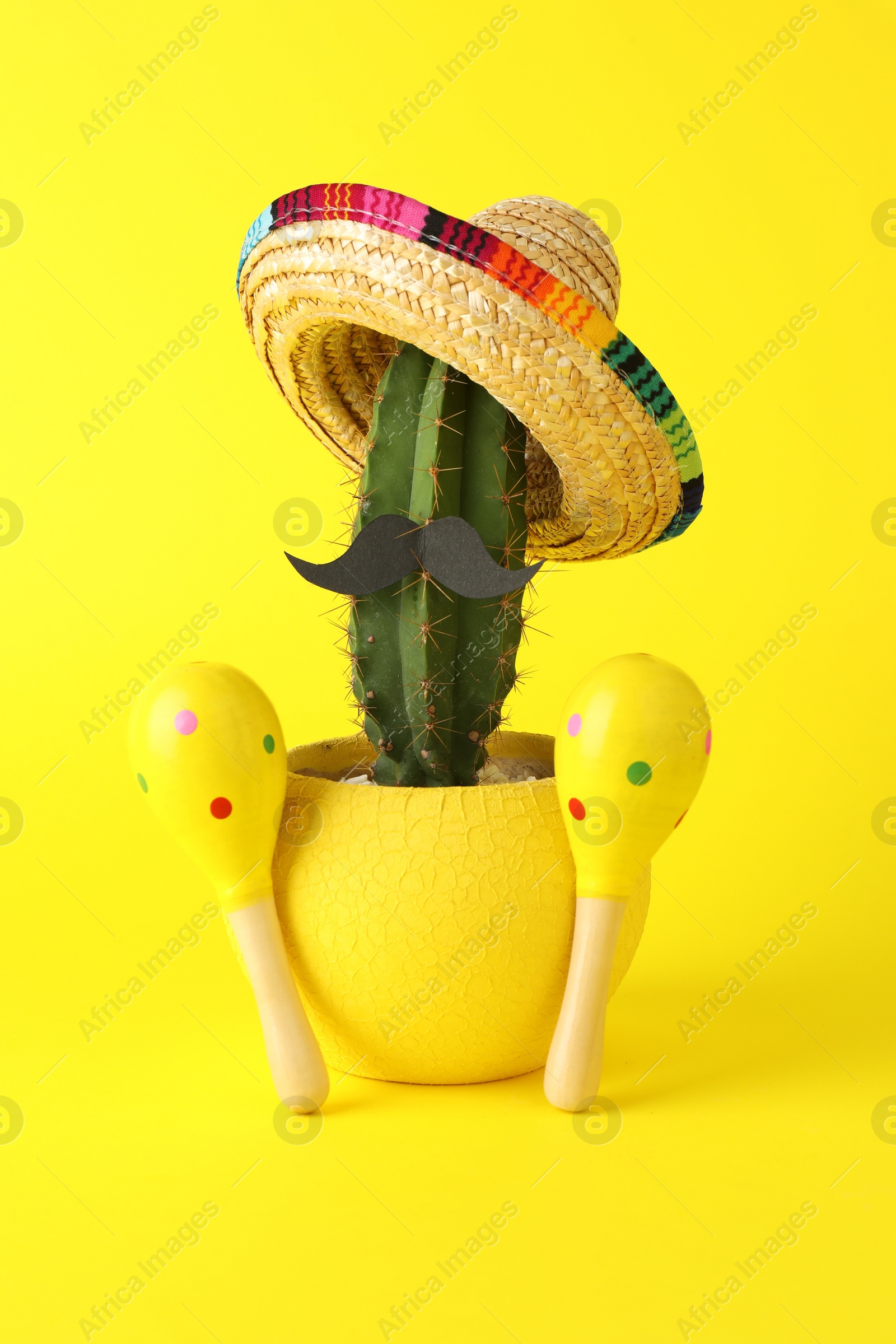 Photo of Cactus with Mexican sombrero hat, fake mustache and maracas on yellow background