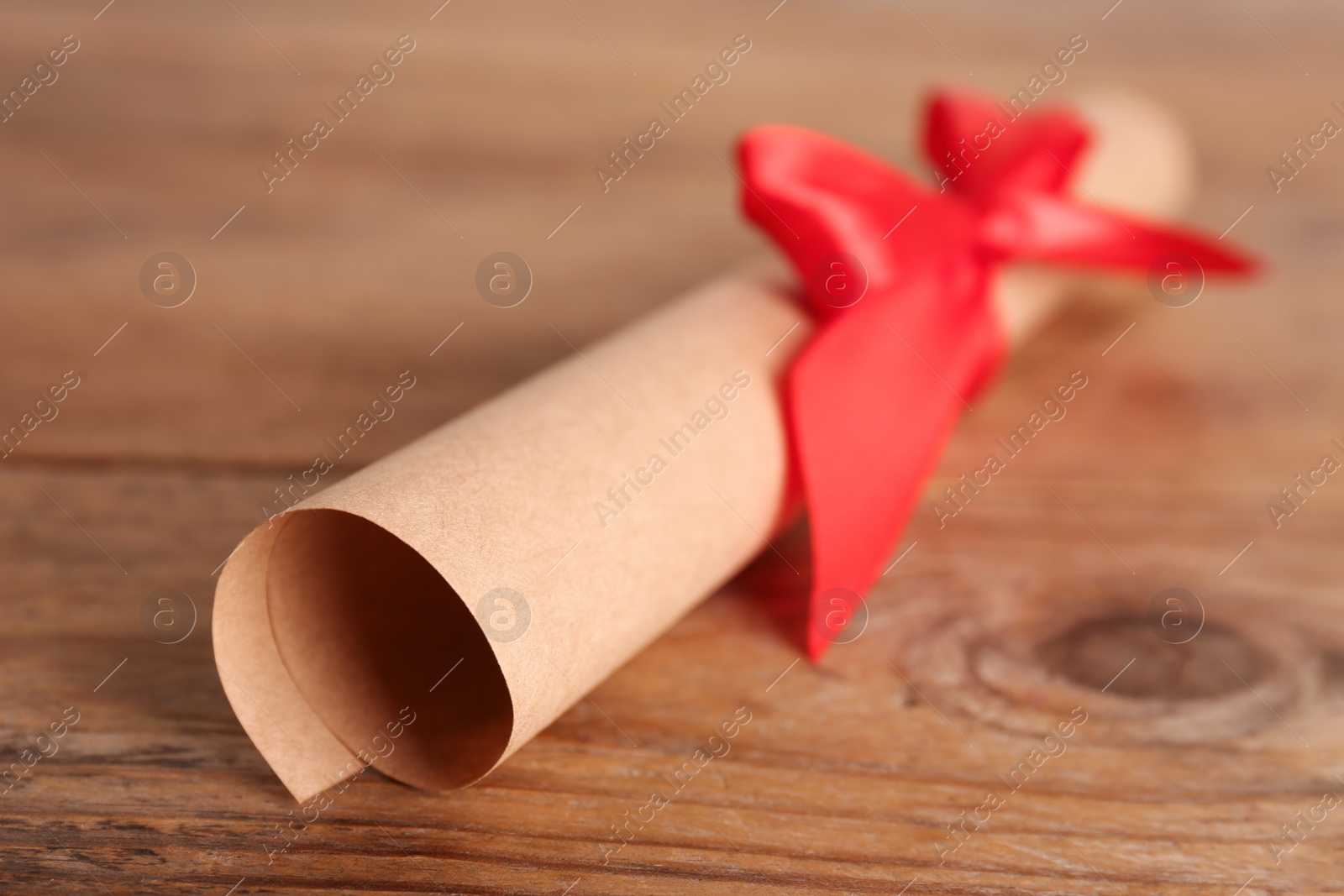 Photo of Rolled student's diploma with red ribbon on wooden table, closeup