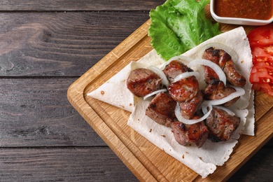 Photo of Wooden board with juicy shish kebab on wooden table