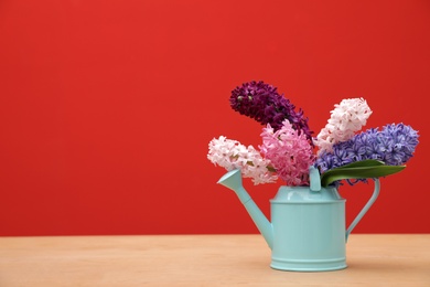 Photo of Beautiful hyacinths in watering can on table against color background, space for text. Spring flowers