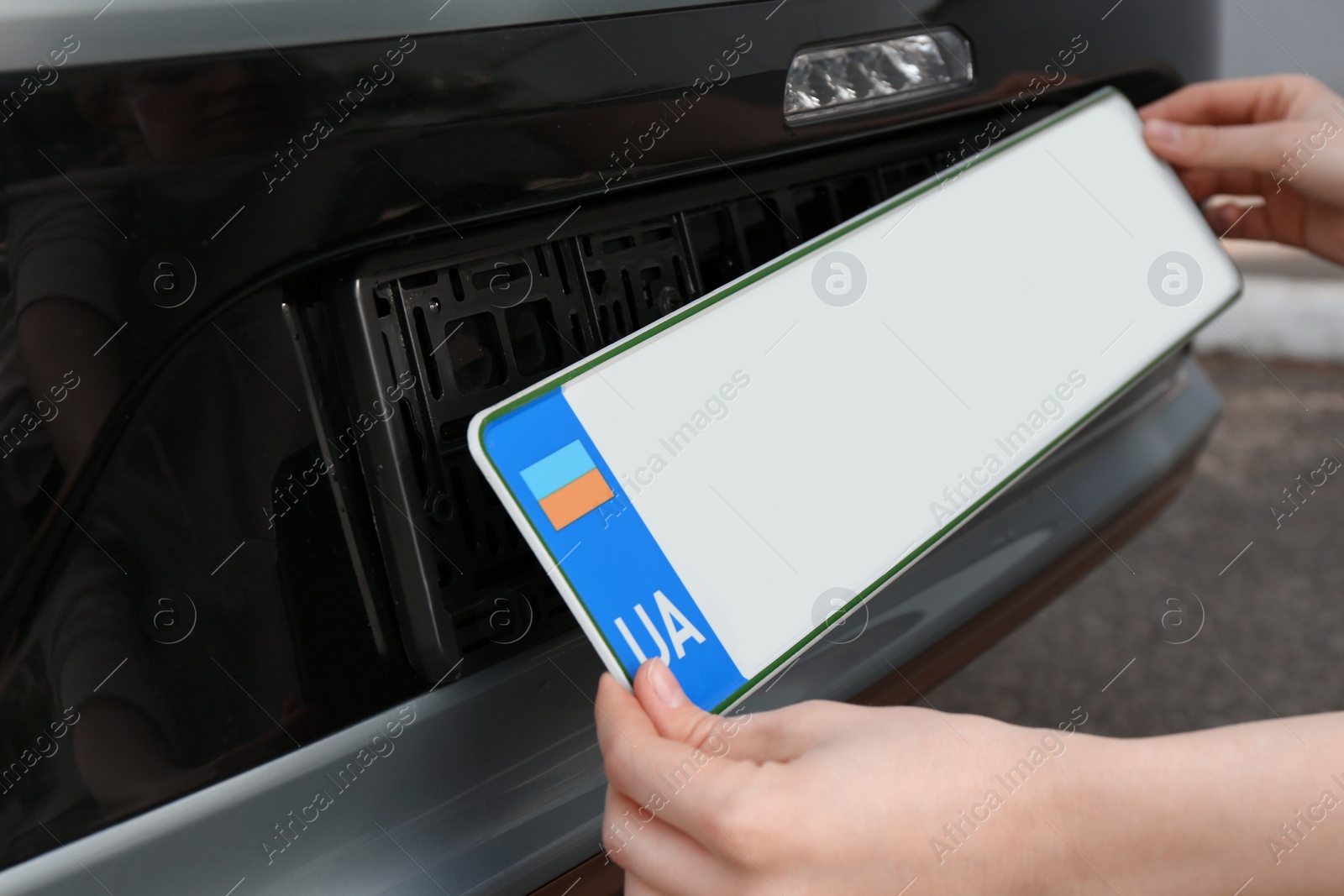 Photo of Woman installing vehicle registration plate outdoors, closeup