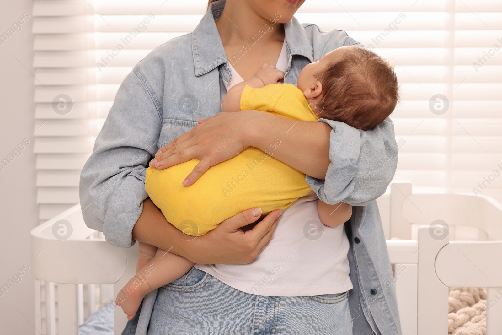 Photo of Mother holding her sleeping newborn baby in child's room, closeup