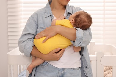 Mother holding her sleeping newborn baby in child's room, closeup