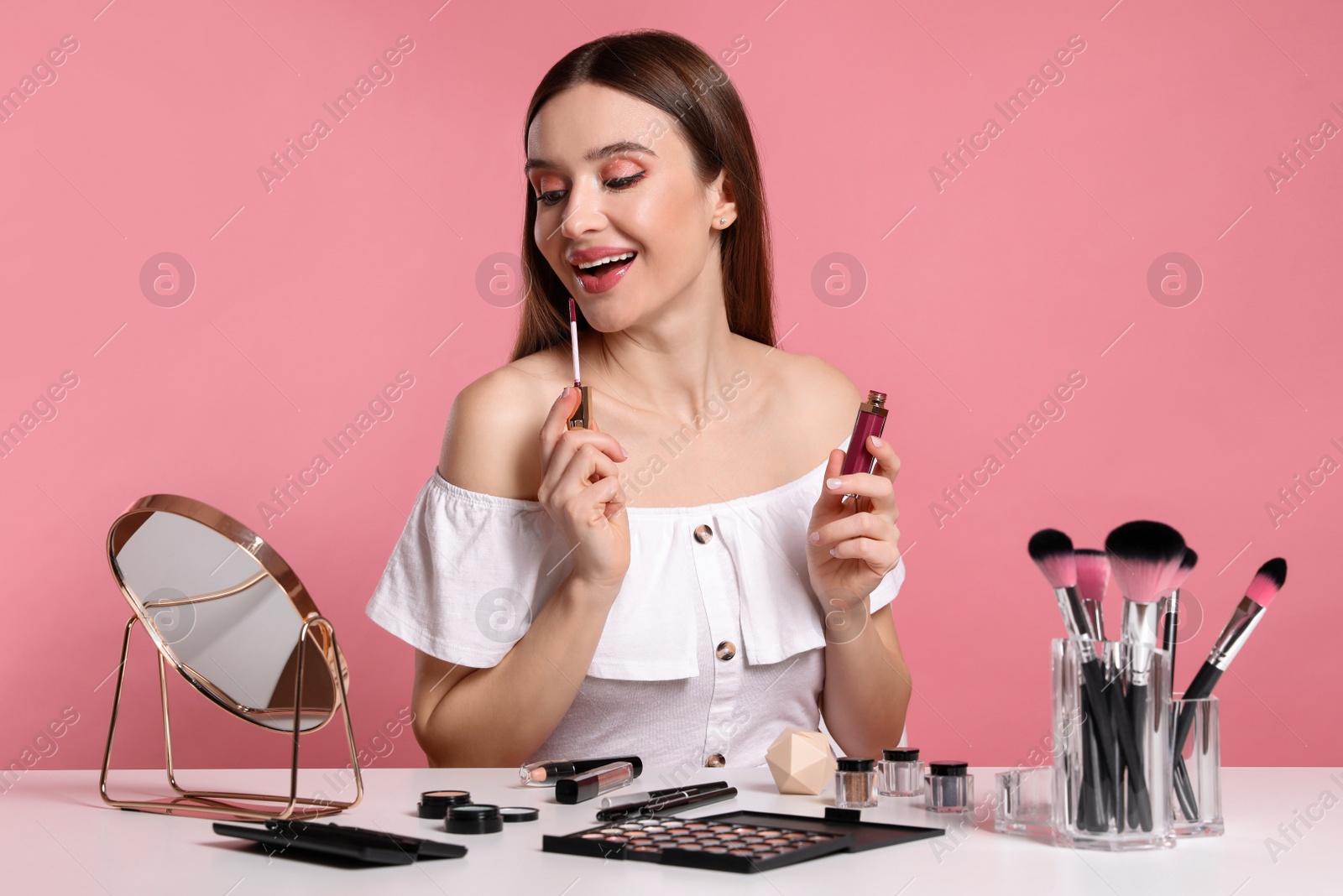 Photo of Beauty blogger applying lipgloss on pink background