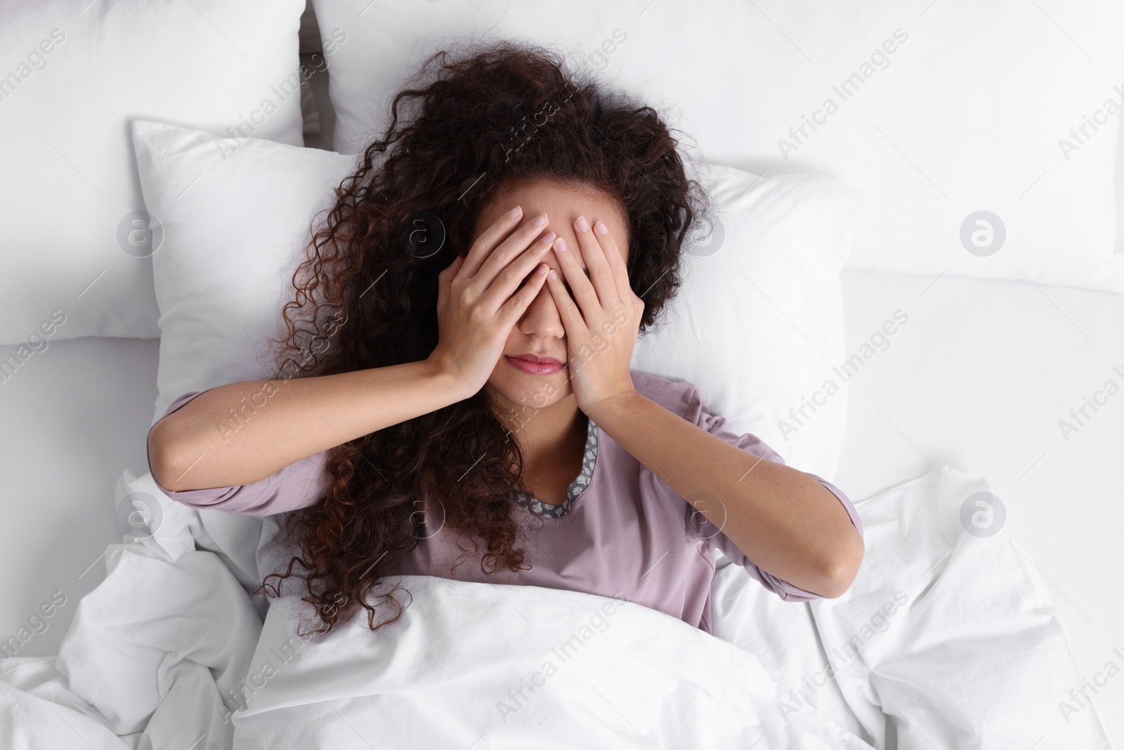 Photo of African American woman covering her face while lying in bed, top view