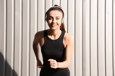 Photo of Young woman in sportswear with headphones near corrugated metal wall