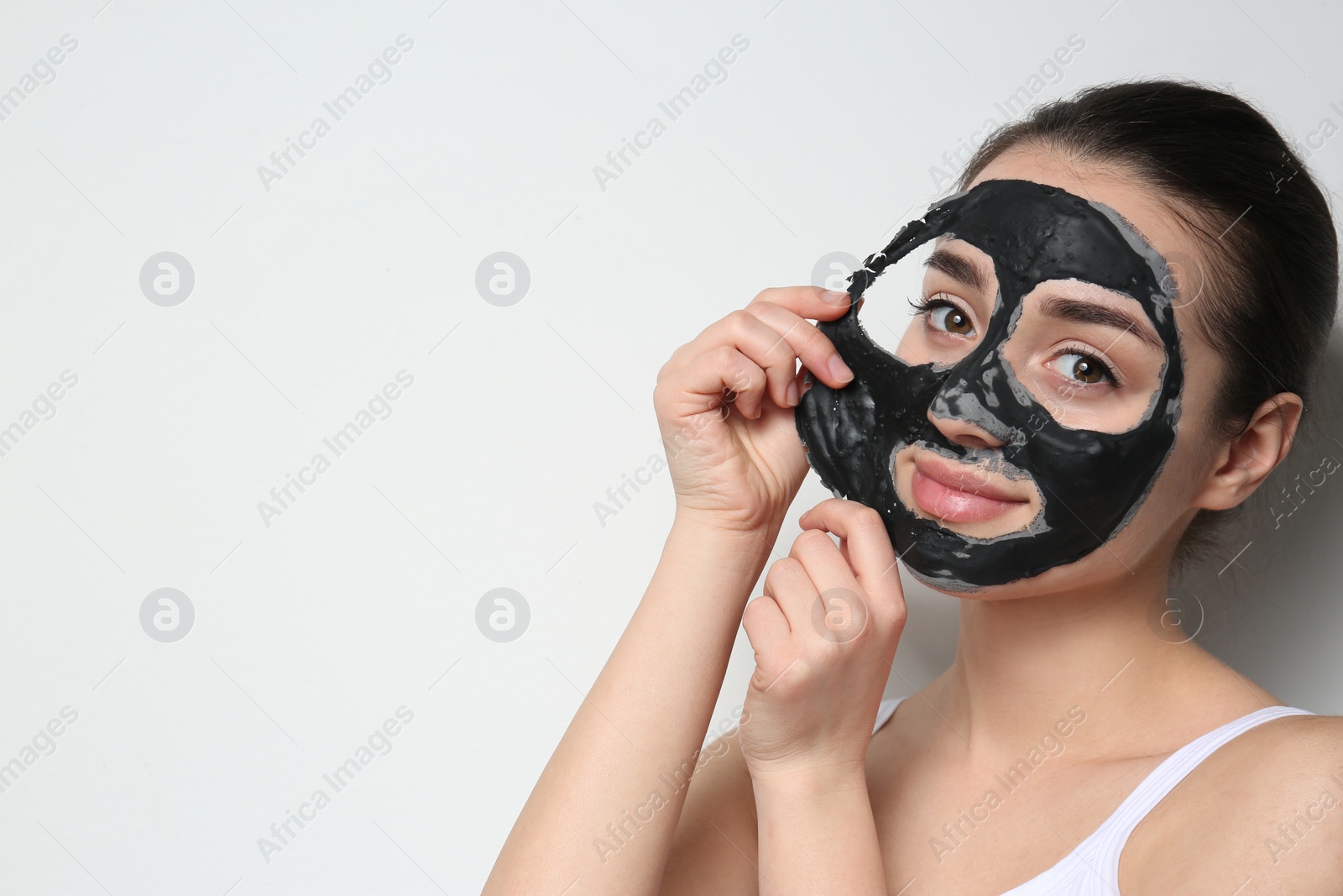 Photo of Beautiful young woman removing black mask from her face on white background. Space for text