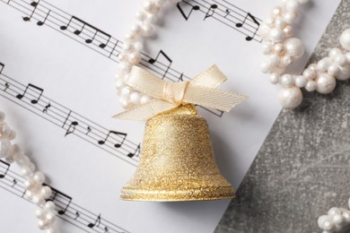 Photo of Golden shiny bell with bow and music sheet on light gray table, flat lay. Christmas decoration