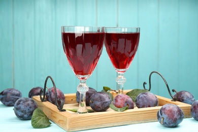 Photo of Delicious plum liquor and ripe fruits on table against light blue background. Homemade strong alcoholic beverage