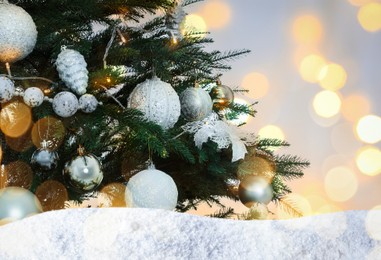 Beautifully decorated Christmas tree and snow on light background. Bokeh effect