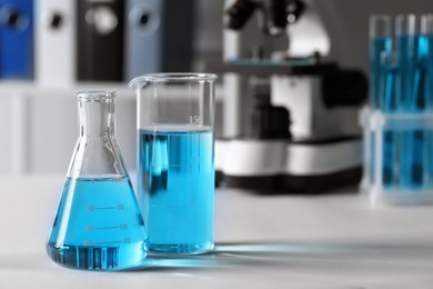 Different laboratory glassware with light blue liquid on table. Space for text