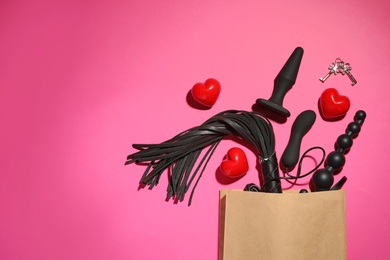 Paper shopping bag with different sex toys on pink background, flat lay. Space for text