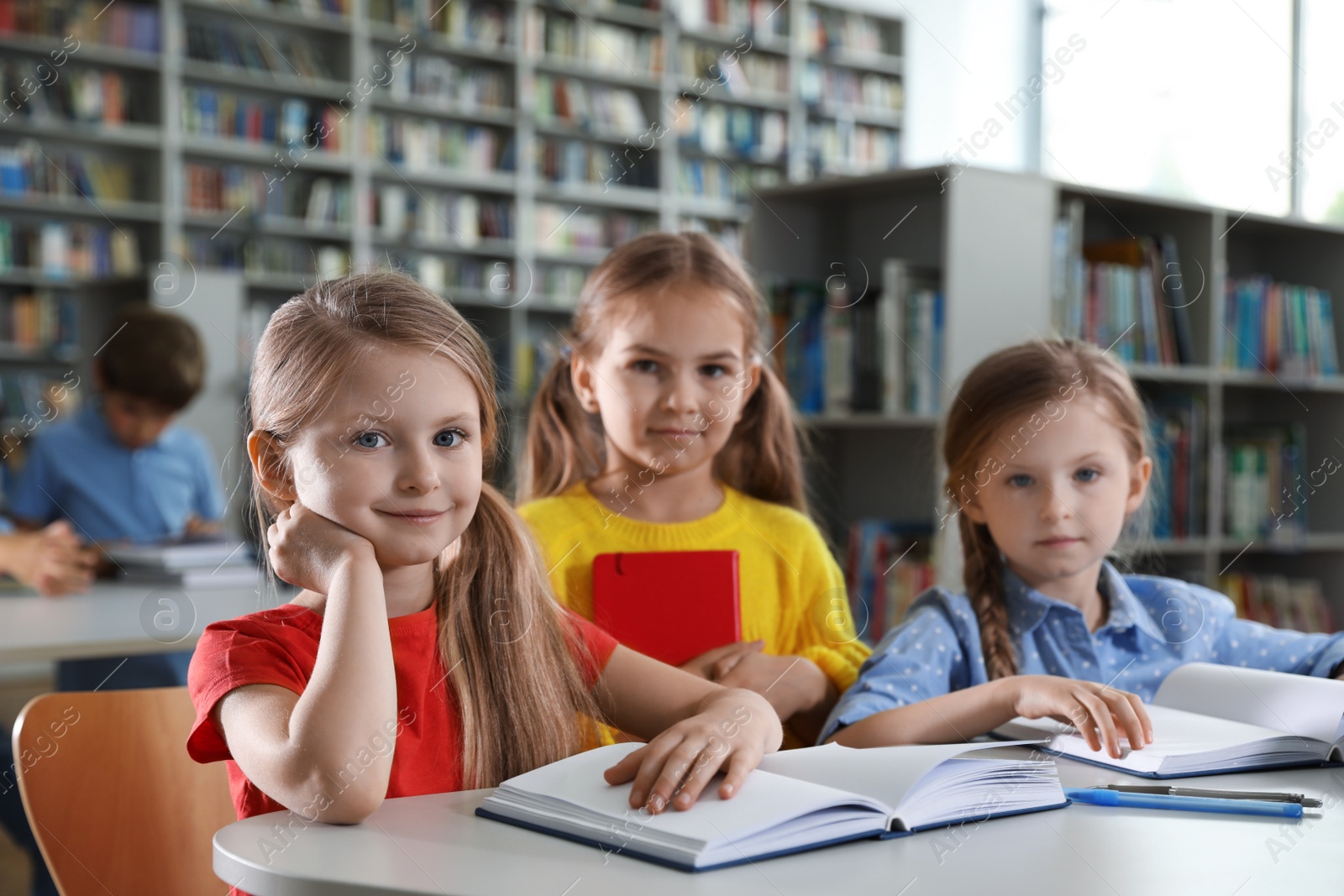 Photo of Happy little girls reading books at table in library