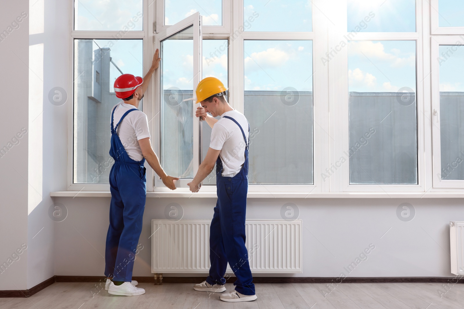 Photo of Workers in uniform installing plastic window indoors