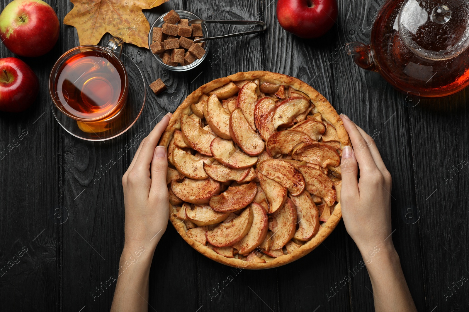 Photo of Woman with delicious apple pie at black wooden table, top view