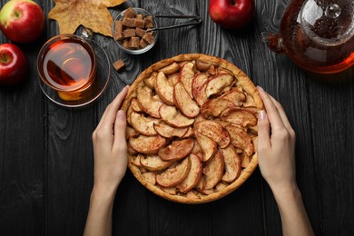Photo of Woman with delicious apple pie at black wooden table, top view