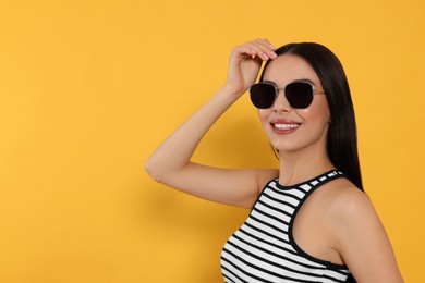 Photo of Attractive happy woman in fashionable sunglasses against orange background. Space for text