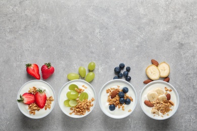 Photo of Bowls with yogurt, granola and different fruits on gray background, top view