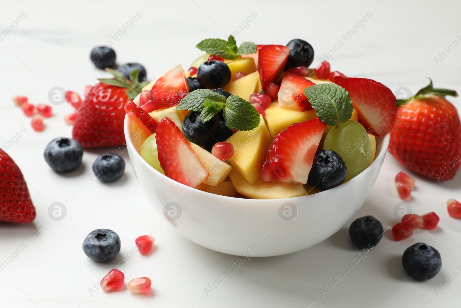Photo of Tasty fruit salad in bowl and ingredients on white table, closeup